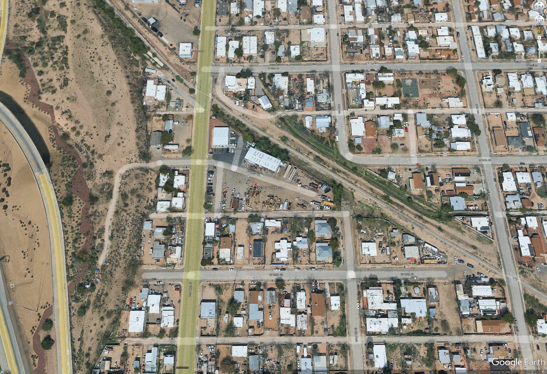 Aerial view of the block at 2425 S. 10th Avenue, South Tucson. The Magnum Paving lot — visible in the upper center with stacked equipment, paving vehicles, and material yards — is the only non-residential parcel on this side of S. 10th Avenue. Every other structure visible in the frame is a single-family home.